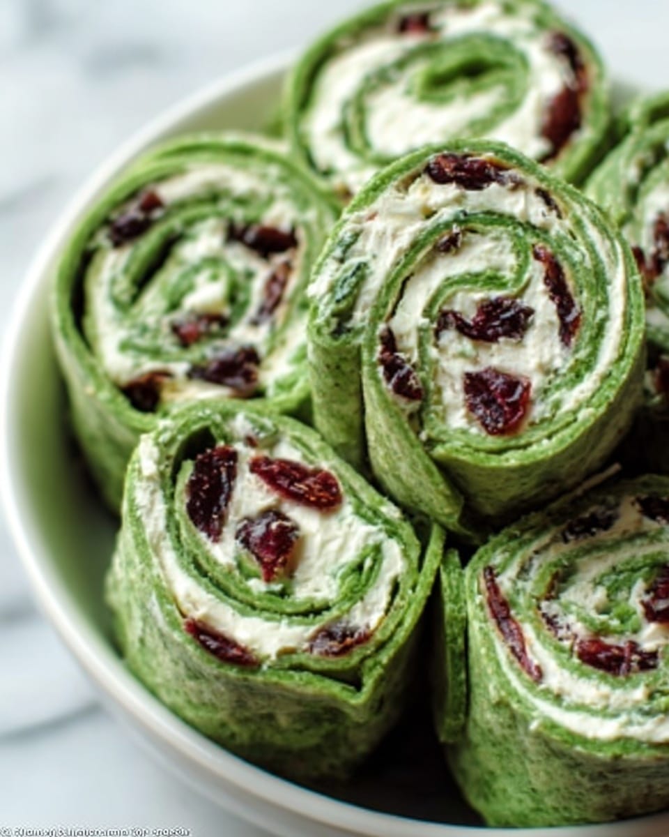 The image shows a close-up of green spinach tortilla roll-ups arranged in a white bowl. Each roll has three visible layers: the bright green outer tortilla, a creamy white spread in the middle, and small pieces of dark red dried cranberries mixed with green leafy bits, all wrapped tightly. The texture of the spinach tortilla looks soft and smooth, and the creamy filling appears thick and evenly spread. The roll-ups are stacked, some tilted, filling the bowl evenly with a fresh and colorful look. The background is a white marbled texture. photo taken with an iphone --ar 4:5 --v 7