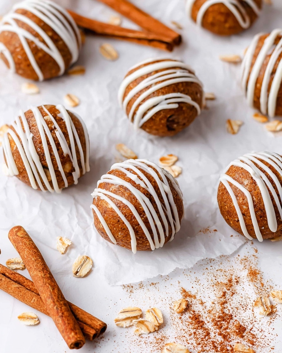 The image shows several round, brown cookie balls with a smooth texture and small oat flakes inside. Each cookie is decorated with thin, white icing lines draped across the top in a neat, diagonal pattern. The cookies rest on a crinkled white paper surface that has some scattered oat flakes and two cinnamon sticks lying nearby with a light dusting of cinnamon powder around them. The overall setting is clean with a white marbled texture background visible beneath the paper. photo taken with an iphone --ar 4:5 --v 7