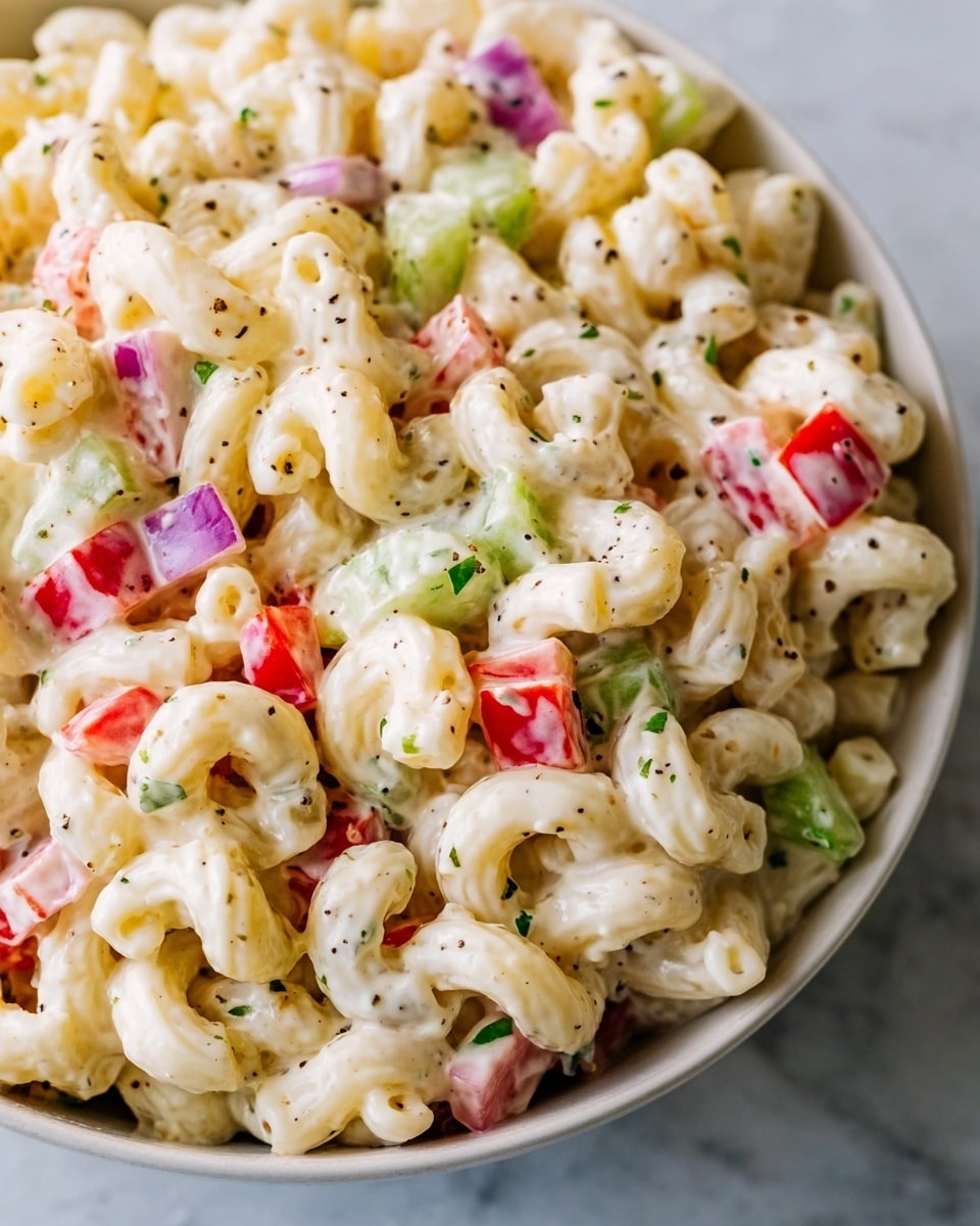 A close-up of a creamy macaroni salad made with elbow-shaped pasta, coated in a smooth white dressing. Mixed within the pasta are small pieces of red bell pepper, purple onion, and green celery, adding bright colors and crunchy textures. Tiny bits of green herbs and black pepper are sprinkled throughout the dish, giving it a fresh and speckled look. The salad sits on a white marbled surface. photo taken with an iphone --ar 4:5 --v 7