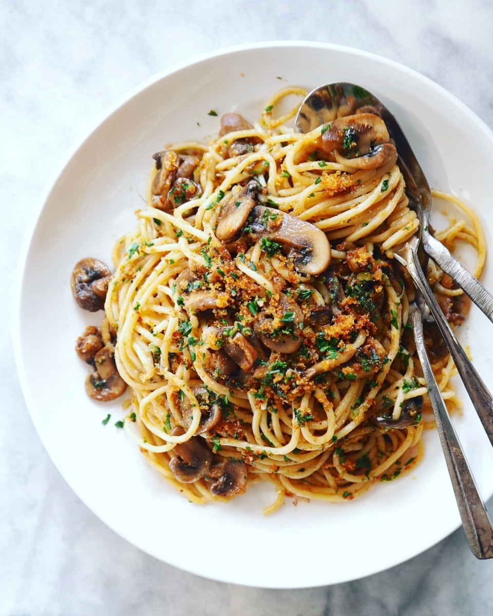 A white plate holds a serving of spaghetti mixed with sliced brown mushrooms and bits of golden breadcrumbs, all tossed together with small green herb flakes scattered on top. A metallic fork and spoon rest crossed on the edge of the plate. The whole setting is on a white marbled texture. photo taken with an iphone --ar 4:5 --v 7