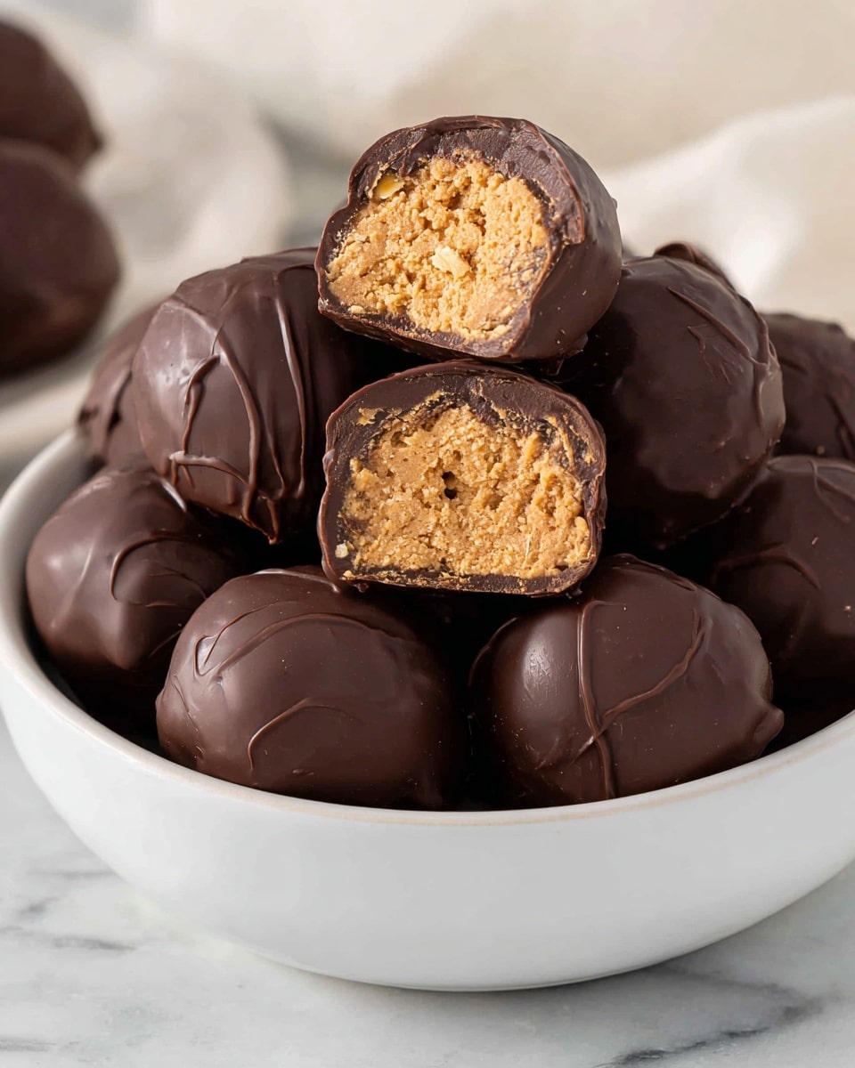 A white bowl filled with several round chocolate-covered peanut butter balls, each coated with a smooth dark brown chocolate layer with slight swirls and shine on the surface. On top, two peanut butter balls are cut in half, showing three main layers: a thin, shiny dark chocolate outer shell; underneath, a thick, light tan peanut butter and oats filling with a slightly crumbly texture; and the base also covered in chocolate, supporting the filling. The bowl rests on a white marbled surface, with soft natural lighting highlighting the chocolate’s gloss and the crunchy texture inside. Photo taken with an iphone --ar 4:5 --v 7