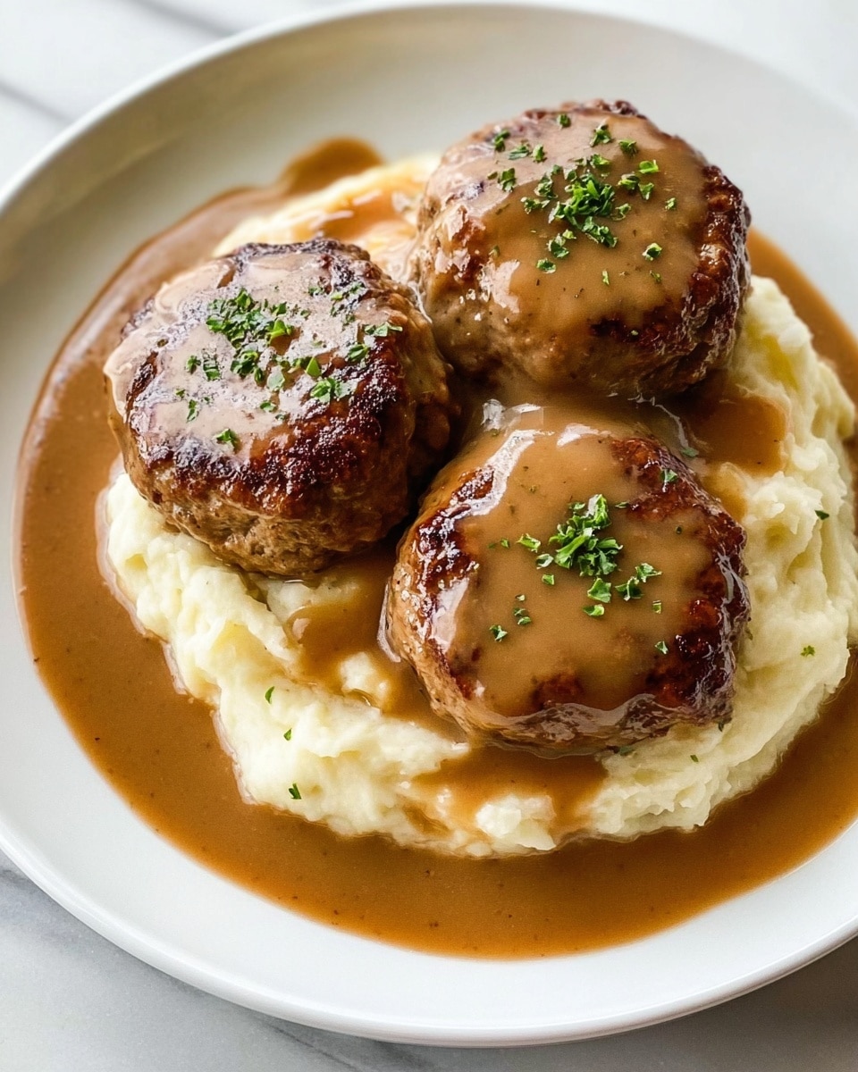 The image shows three round, browned meat patties placed on top of soft, creamy mashed potatoes. Each patty is covered with smooth, rich brown gravy, which also spreads around the base on the white plate. Small bits of green herbs are sprinkled on top of the gravy-covered patties, adding a touch of color. The plate rests on a white marbled surface, creating a clean and bright background. Photo taken with an iphone --ar 4:5 --v 7