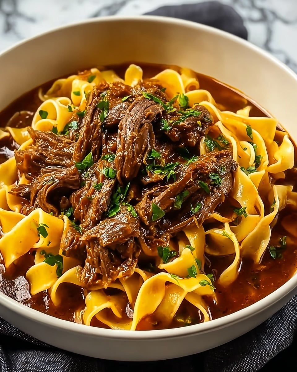 A white bowl filled with wide, flat noodles that have a light yellow color and a soft, slightly curled texture, sitting in a thick, glossy dark brown sauce. On top of the noodles are several pieces of tender, shredded beef that are rich brown with a moist, juicy appearance. The dish is garnished with fresh, chopped green herbs scattered over the beef, adding a bright contrast. The bowl is resting on a white marbled surface with a dark cloth partially visible underneath. photo taken with an iphone --ar 4:5 --v 7