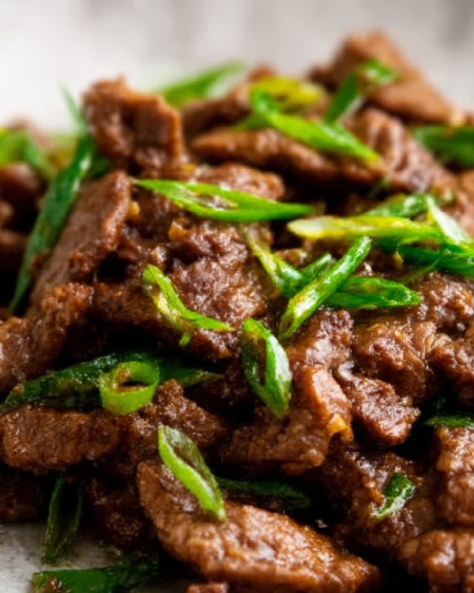 The dish shows a close-up of tender beef strips cooked in a dark brown sauce that looks glossy and rich. Bright green scallion pieces are scattered on top, adding a fresh color contrast. The beef has a soft, juicy texture with some sauce clinging to it, and the background features a white marbled surface. The image looks warm and appetizing with steam rising softly. Photo taken with an iphone --ar 4:5 --v 7
