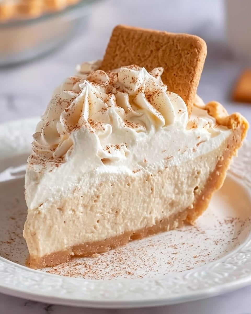 A thick slice of pie with three visible layers sits on a white plate with delicate patterns. The bottom layer is a pale, golden-brown flaky crust. Above that is a thick, creamy beige filling with a smooth texture. The top layer is a generous amount of white whipped cream, decorated with light swirls and a sprinkle of cinnamon powder. A rectangular biscuit with a rough texture and brown color is placed upright on the cream. The scene has a soft light with a white marbled surface in the background. Photo taken with an iphone --ar 4:5 --v 7