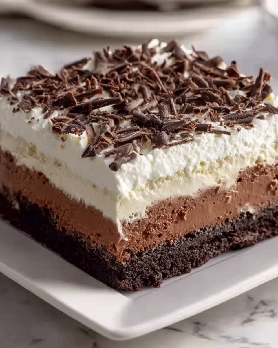The image shows a square dessert with three thick layers on a white square plate placed on a white marbled surface. The bottom layer is a dark, crumbly crust, almost black in color, with a slightly rough texture. Above it is a thick middle layer of smooth, creamy milk chocolate that looks firm and rich. The top layer is a thick, fluffy, light cream color with soft, uneven peaks. On the surface of the cream layer, there are scattered dark chocolate shavings that add texture and contrast. photo taken with an iphone --ar 4:5 --v 7