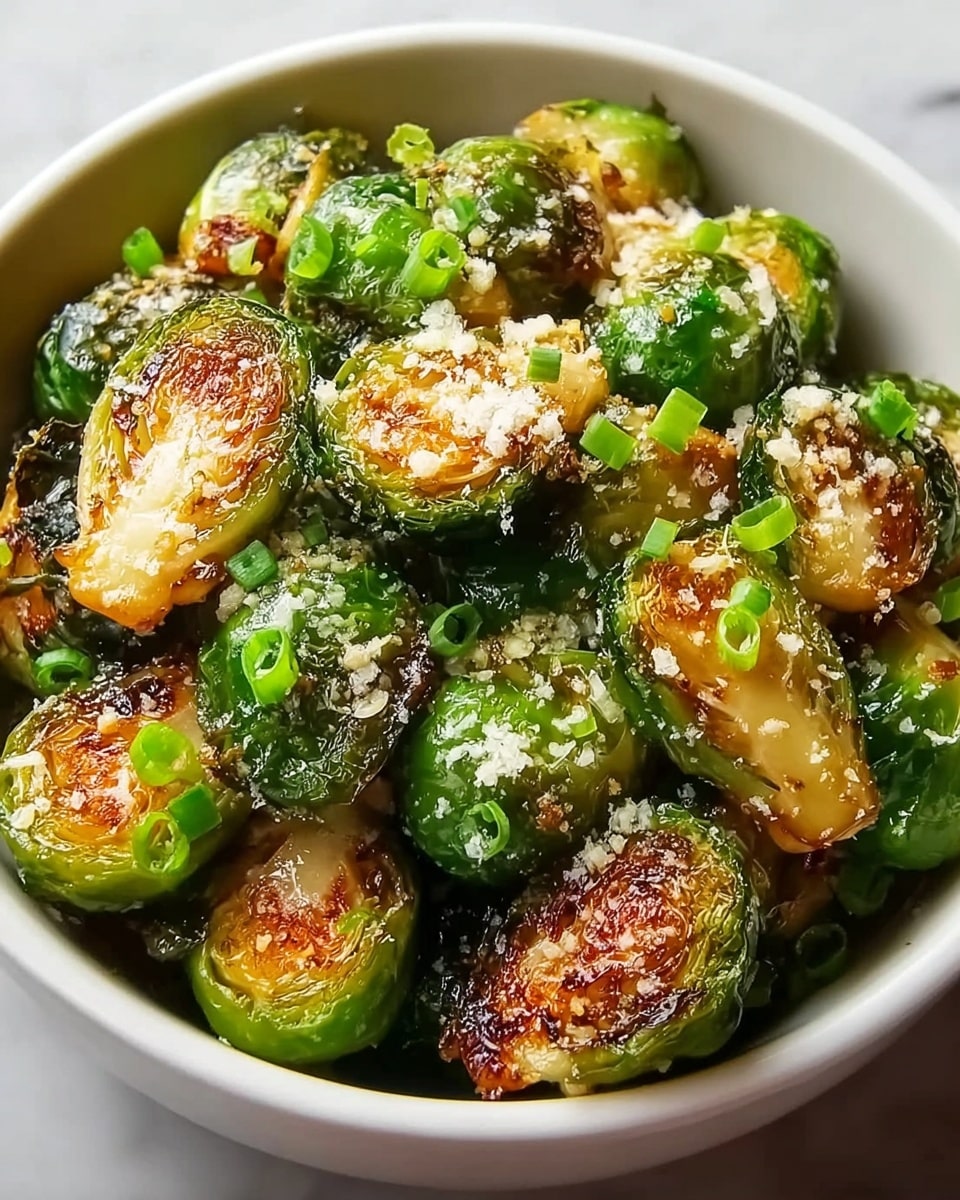The image shows a white bowl filled with roasted Brussels sprouts cut in halves, with a golden-brown crispy texture on the flat side and a bright green color on the rounded leafy side. The Brussels sprouts are sprinkled with finely grated cheese that melts slightly over the warm surfaces, and small pieces of green onion are scattered on top, adding a fresh green contrast. The bowl is set on a white marbled surface. photo taken with an iphone --ar 4:5 --v 7