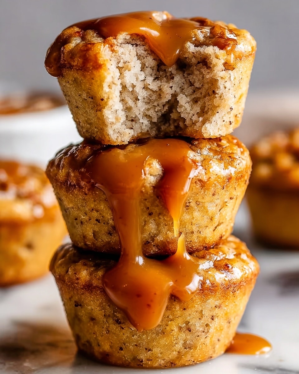 The image shows a stack of three small muffins placed on a white marbled surface, all covered in a thick, glossy caramel sauce that drips down the sides. The top muffin has a bite taken out of it, revealing a soft and moist interior with a light beige crumb and small bits inside, suggesting a textured filling. The muffins are golden brown on the outside with a slightly rough texture, and the caramel sauce shines with a rich amber color. The background is blurred with a warm tone, focusing attention on the muffins. photo taken with an iphone --ar 4:5 --v 7