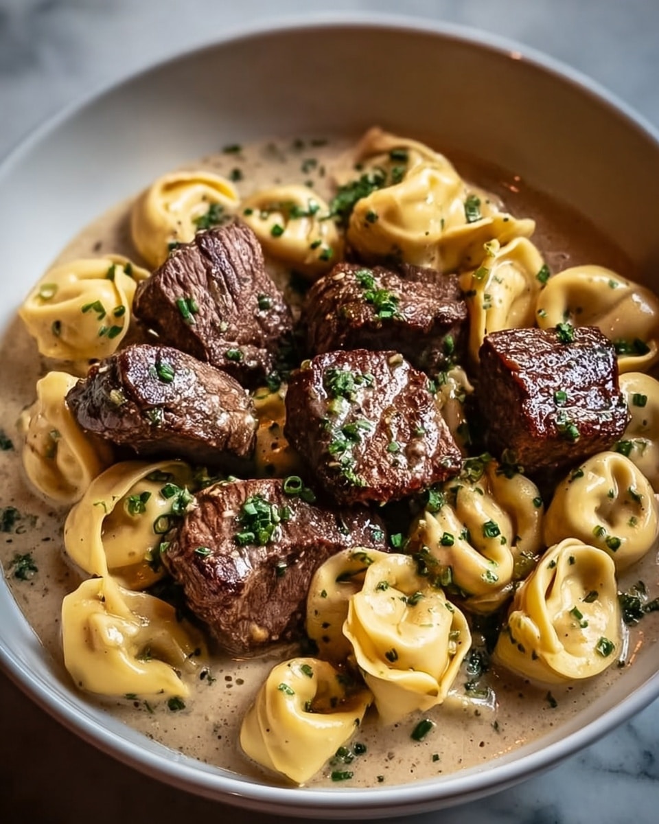 A white bowl filled with two main layers: the bottom layer is creamy, light beige sauce with smooth texture, and the top layer consists of golden-yellow tortellini arranged evenly around thick, juicy brown steak cubes with a seared, slightly crispy surface. Both tortellini and steak pieces are sprinkled with small chopped green herbs, adding a fresh touch. The bowl sits on a white marbled textured surface. Photo taken with an iphone --ar 4:5 --v 7