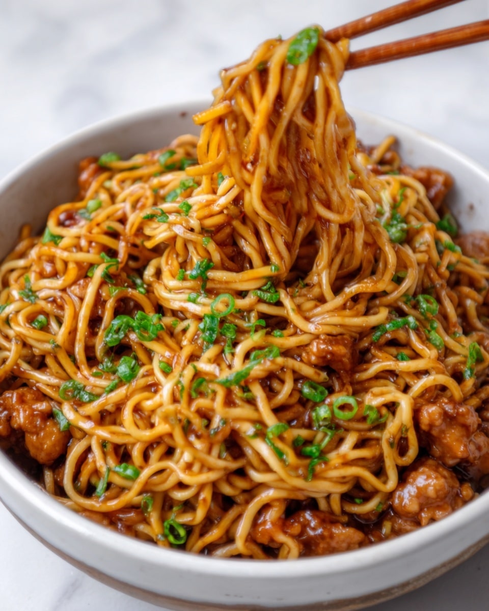 A close-up of a white bowl filled with cooked noodles mixed with small pieces of cooked meat and sprinkled with chopped green herbs. The noodles are brownish-red with a glossy, oily texture, and the meat pieces are mixed evenly throughout the noodles. Two chopsticks hold some noodles lifted above the bowl, showing the soft texture and slight oil shine. The bowl sits on a white marbled surface. Photo taken with an iphone --ar 4:5 --v 7
