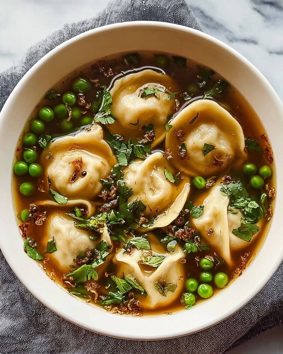 The image shows a white bowl filled with clear brown broth and several light beige dumplings floating on top. The dumplings have soft, slightly wrinkled textures with some darker spots from cooking. Scattered around the dumplings are bright green peas and chopped dark green leafy herbs. Small bits of what looks like fried garlic are sprinkled on the surface, adding texture and contrast. The bowl sits on a gray cloth, all placed on a white marbled surface. photo taken with an iphone --ar 4:5 --v 7